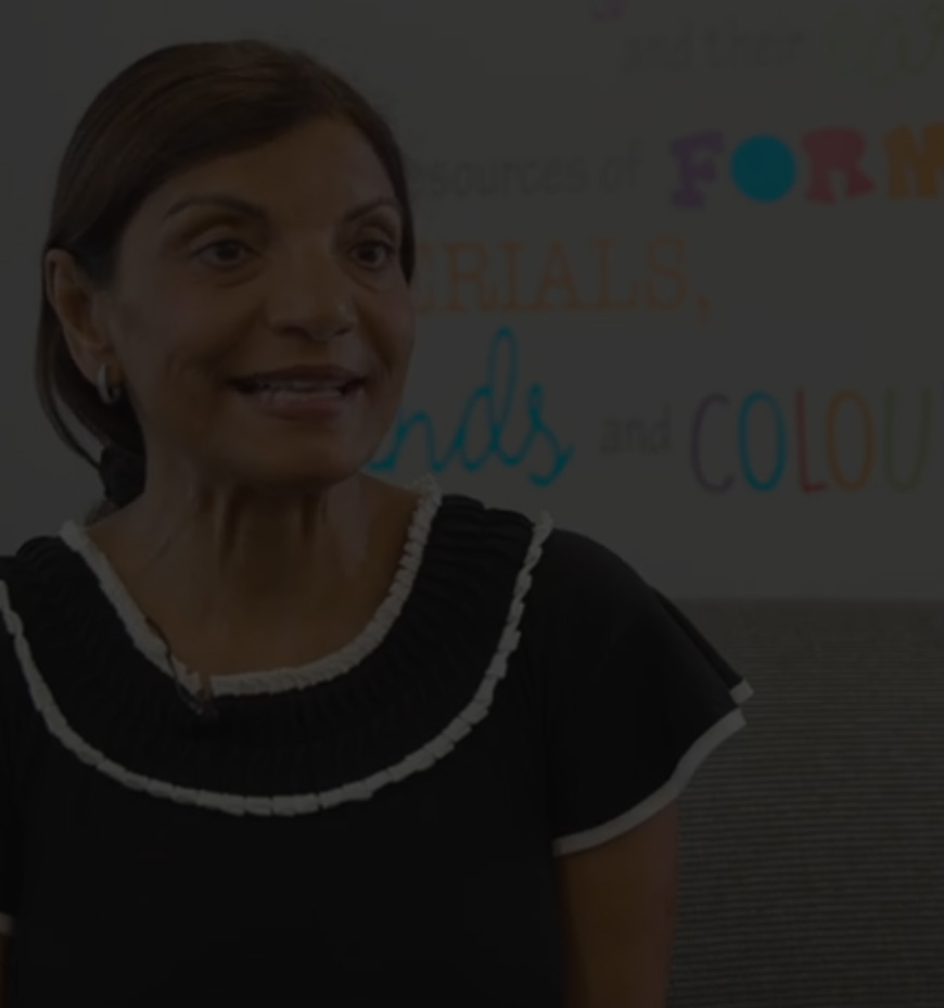 A woman with dark hair and a black top with white trim sits in front of a wall with colorful letters and words, epitomizing the vibrant environment of an early childhood education franchise.