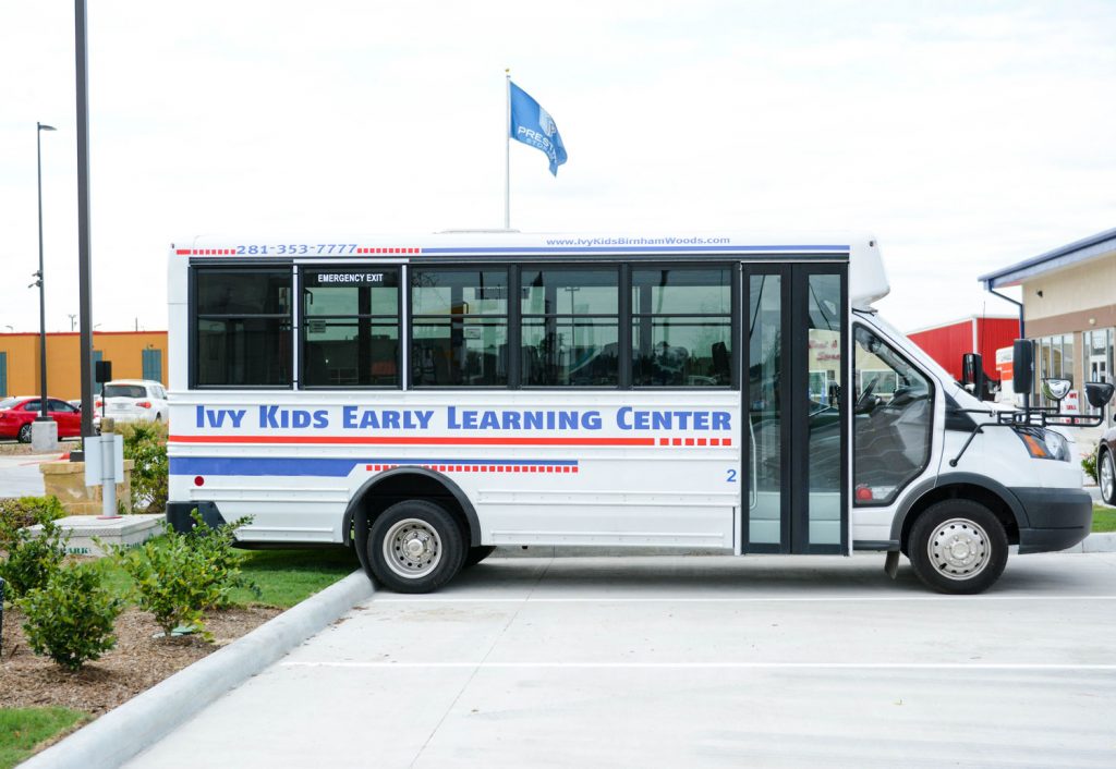 A small white bus with "Ivy Kids Early Learning Center" written on the side, an esteemed preschool franchise, is parked in a parking lot.