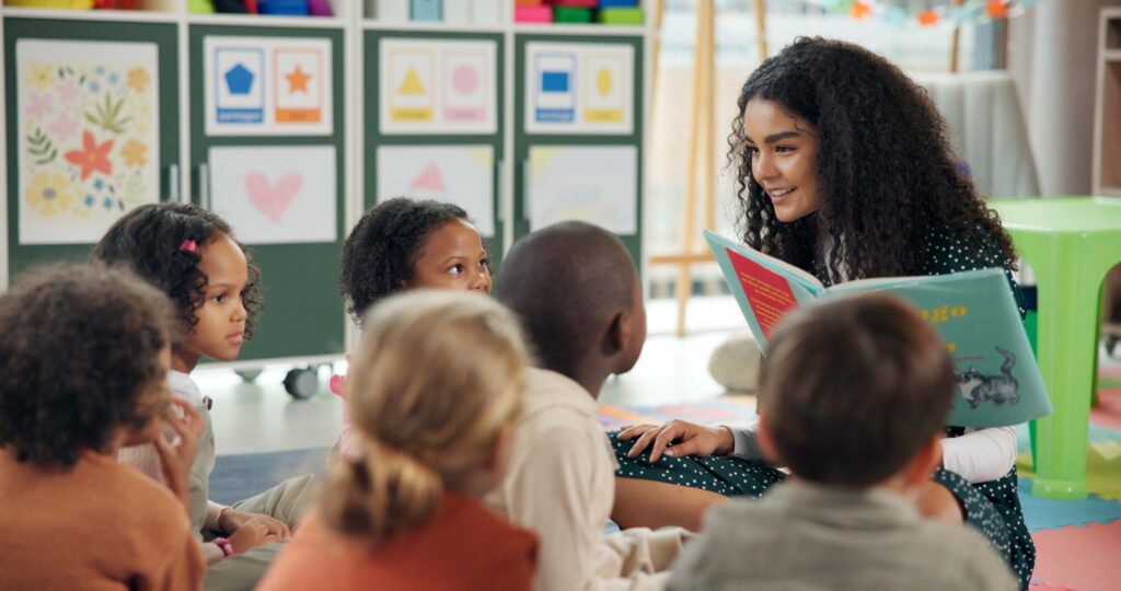 Daycare teacher reading a picture book to a group of young children in a bright classroom, representing the best daycare businesses to own.