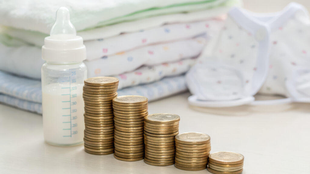 Baby bottle, diapers, and stacked coins representing how much it costs to open a daycare.