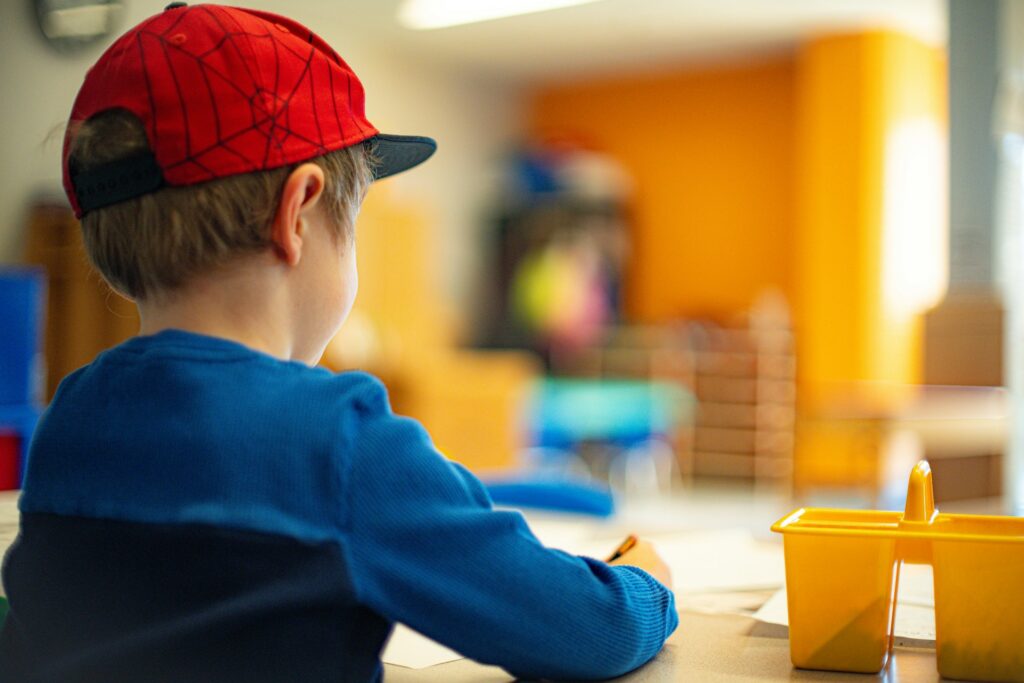 The Difference Between a Daycare Franchise and a Preschool Franchise 2 A child draws at a table while wearing a red hat and blue shirt.